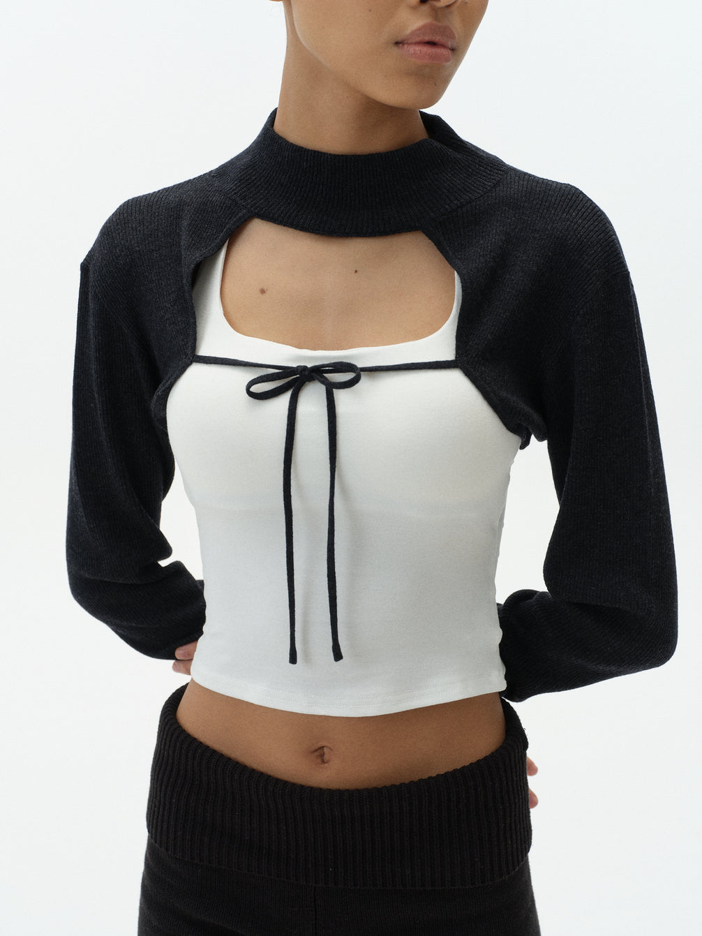Woman wearing a black cardigan over a white top with a black bow on a white background