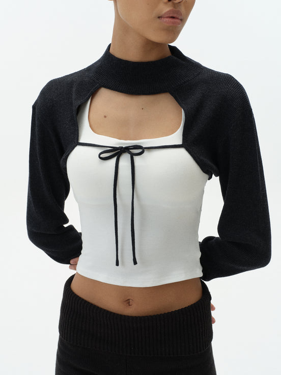Woman wearing a black cardigan over a white top with a black bow on a white background